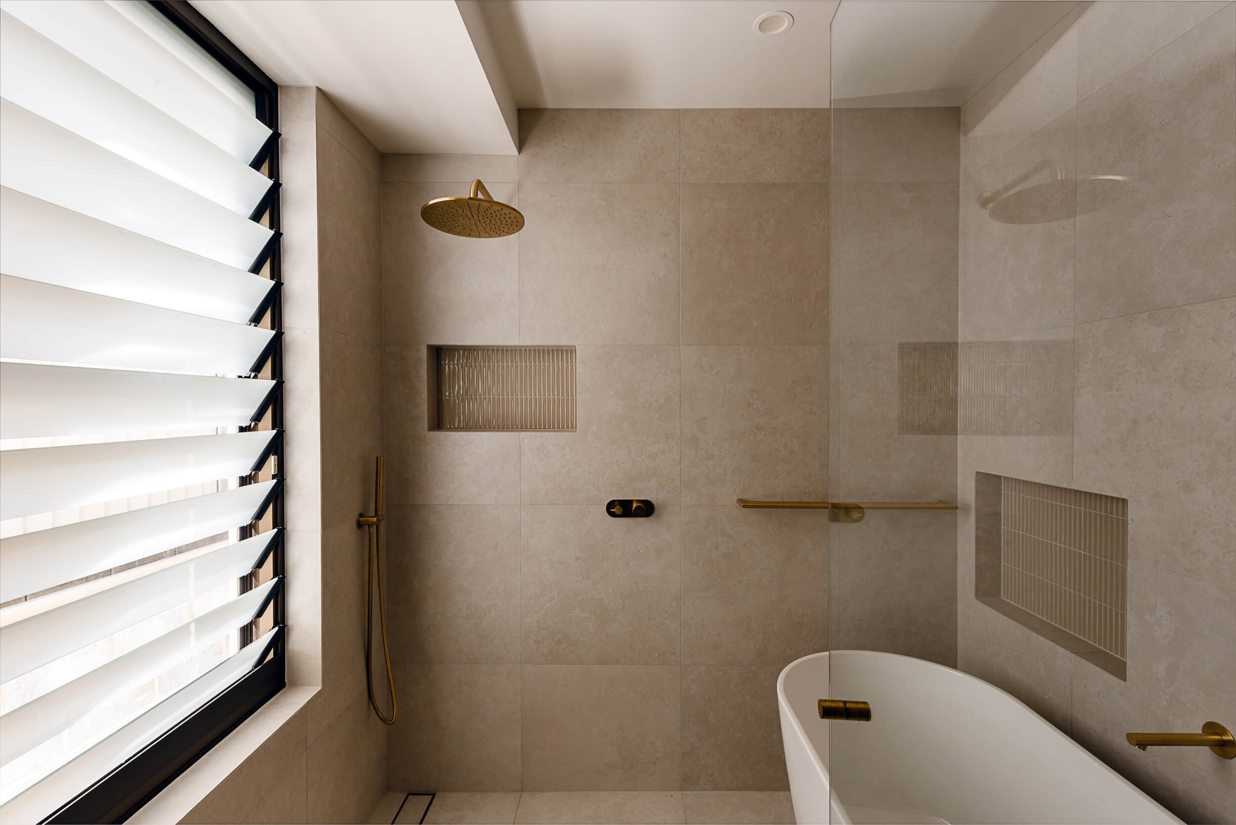 Master bathroom at O'Brien Duplex Bulli with freestanding bathtub, brushed brass tapware, stone wall tiles, and operable louvre privacy window by Kibbin Design and SLD Projects