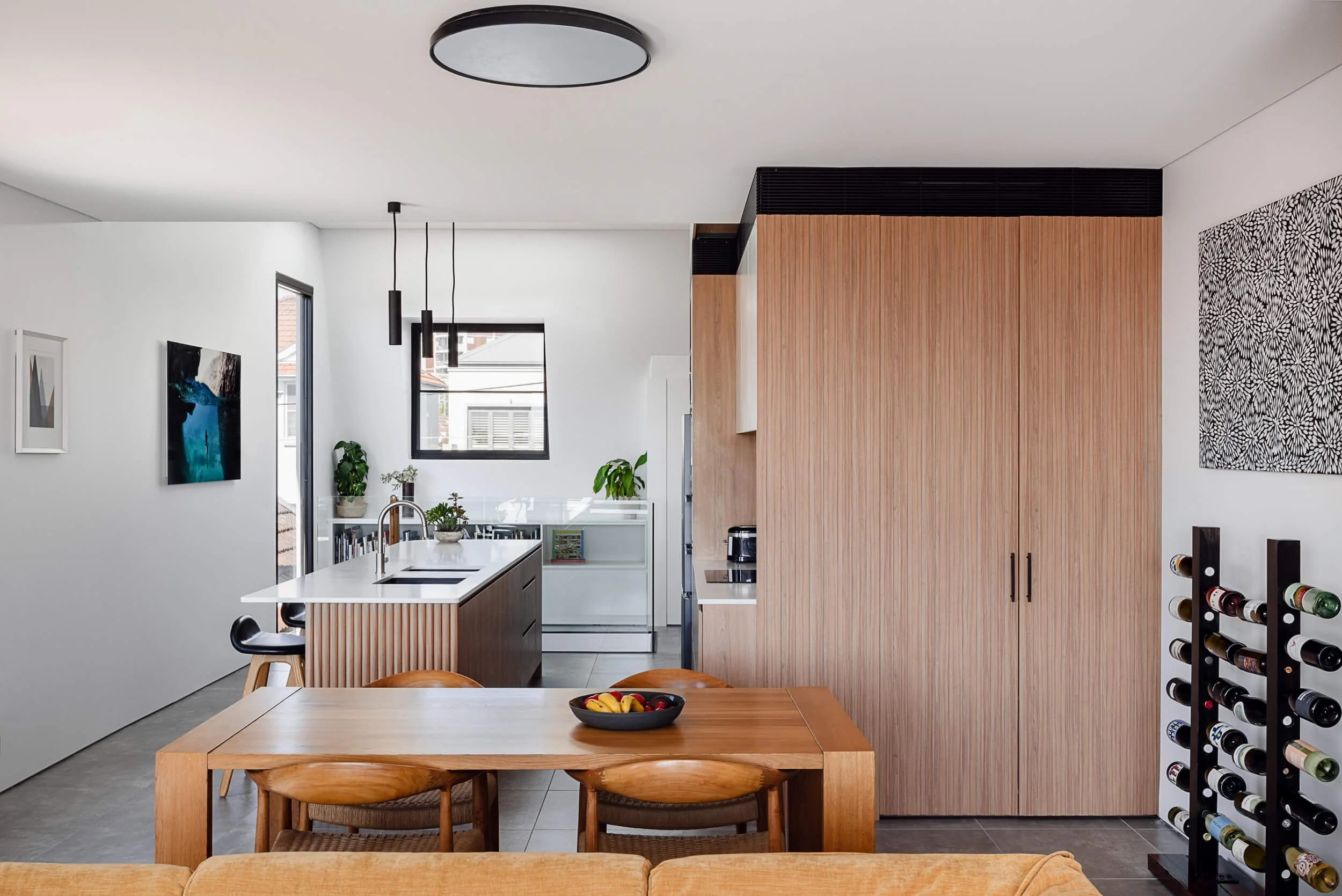 Open-plan kitchen and dining area featuring a ribbed timber island, custom floor-to-ceiling oak joinery, and wooden dining table at Bondi Heights in Sydney, NSW