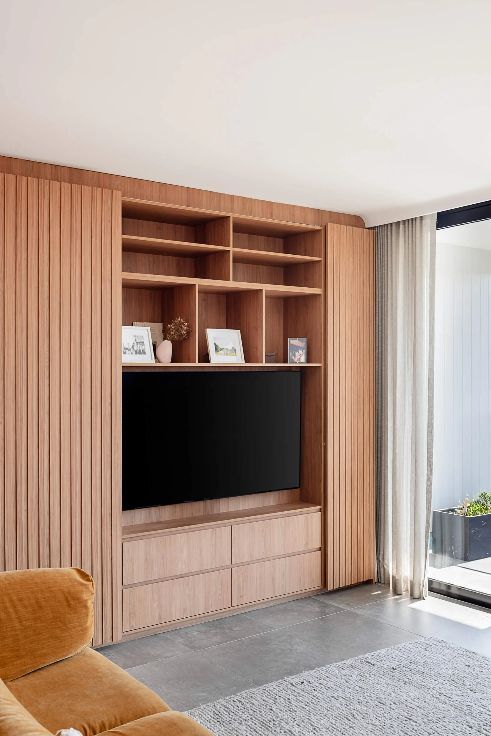 Custom timber batten media cabinetry with open shelving and built-in television in an upper-level living room at Bondi Heights in Sydney, NSW