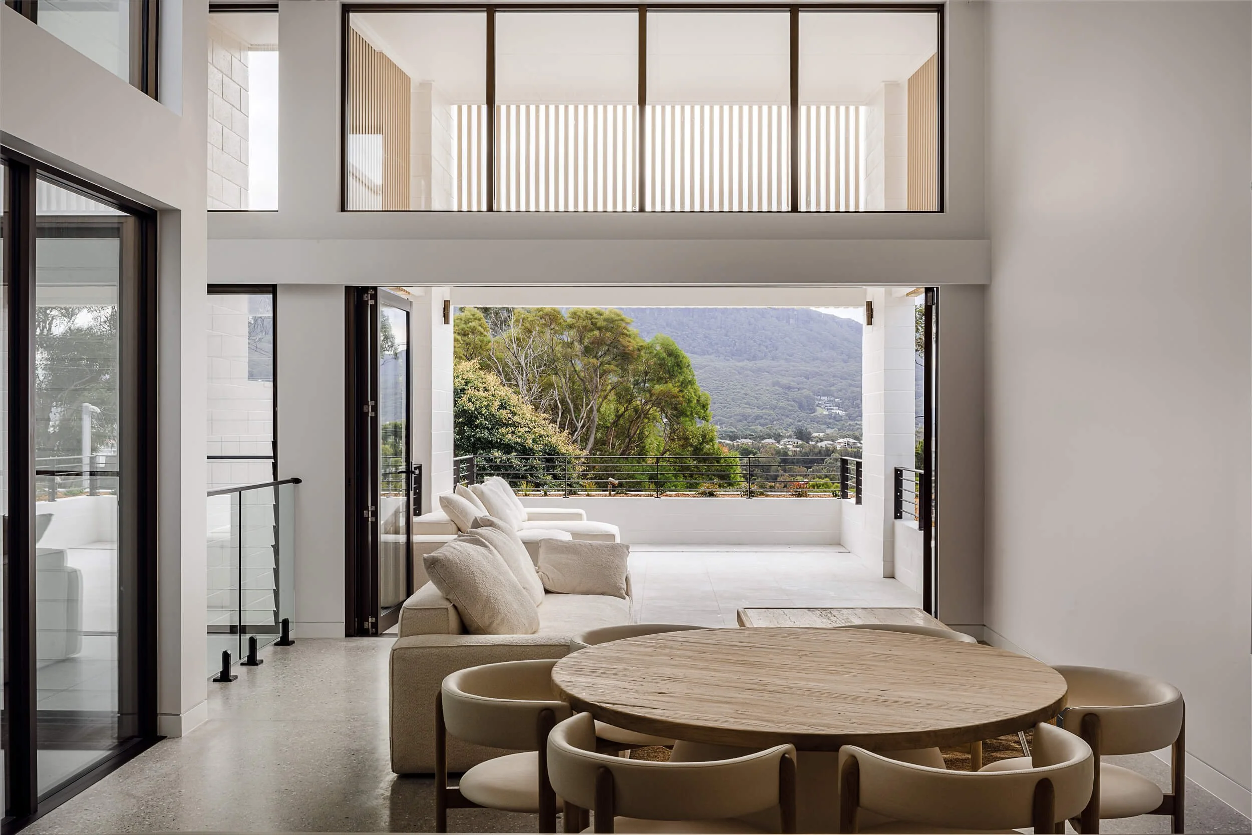 Double-height open plan living and dining space opening to sunlit terrace with sweeping Illawarra escarpment views at O'Brien Duplex Bulli by Kibbin Design and SLD Projects