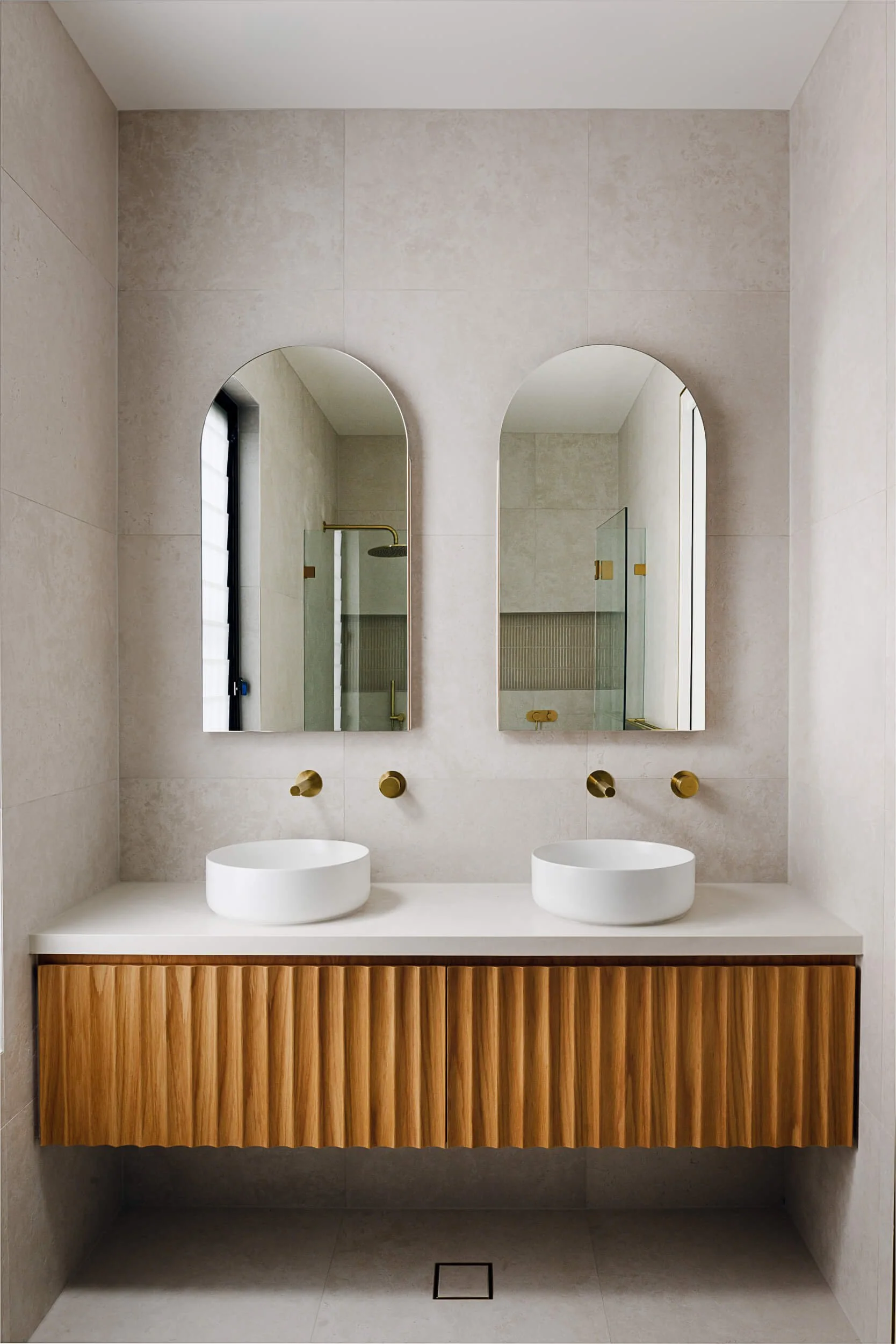 Bespoke master ensuite double vanity with floating fluted timber cabinetry, twin round vessel basins, twin arched mirrors, and brushed brass wall tapware at O'Brien Duplex Bulli by SLD Projects