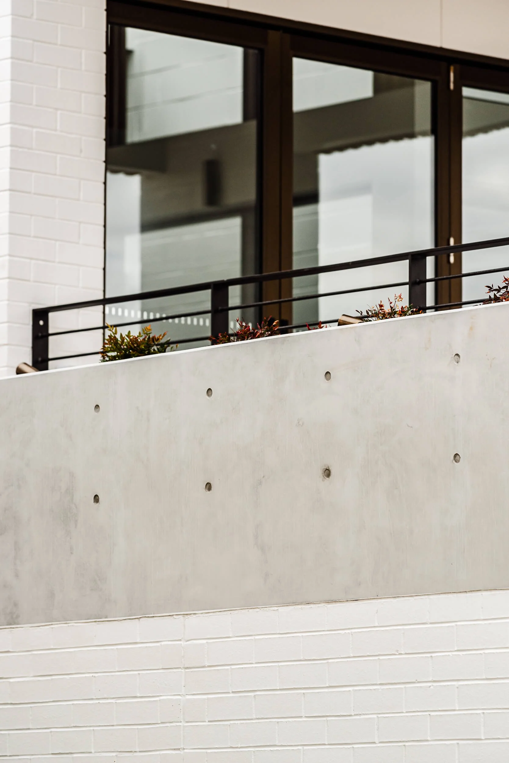 Off-form concrete terrace parapet with architectural tie holes, black steel balustrade, and painted brickwork at O'Brien Duplex Bulli by SLD Projects and Kibbin Design