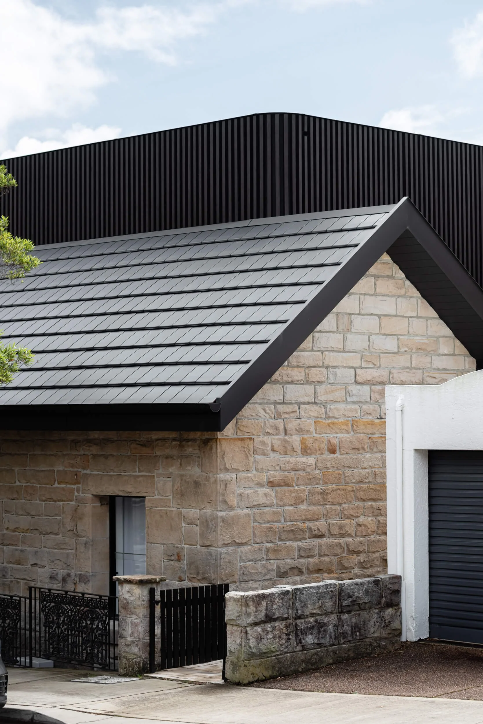 Exterior architectural detail highlighting the contrast between heavy heritage sandstone, a modern dark roof, and black ribbed timber cladding