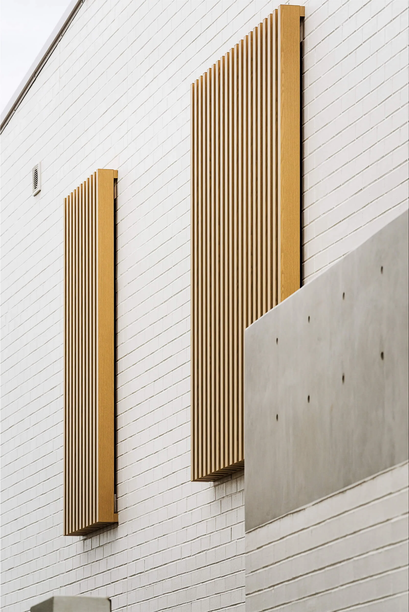 Vertical timber batten sun shading screens mounted to painted white brick facade above concrete terrace parapet at O'Brien Duplex Bulli by Kibbin Design and SLD Projects