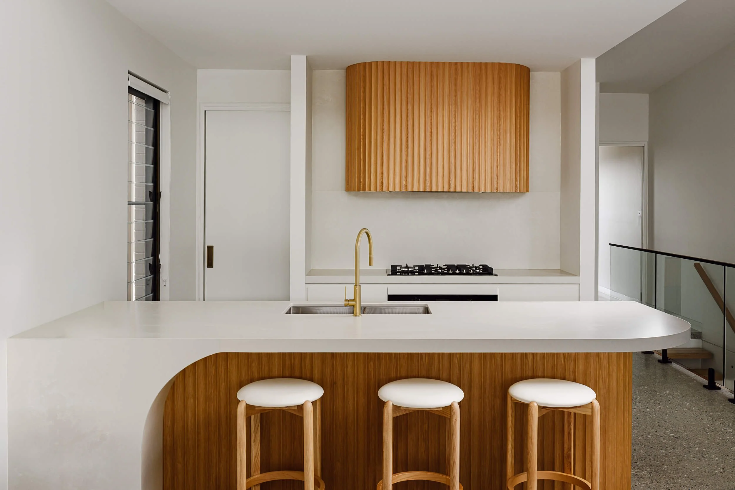 Custom architectural kitchen island with curved fluted timber joinery, white stone waterfall benchtop, and brushed brass gooseneck tapware at O'Brien Duplex Bulli by SLD Projects
