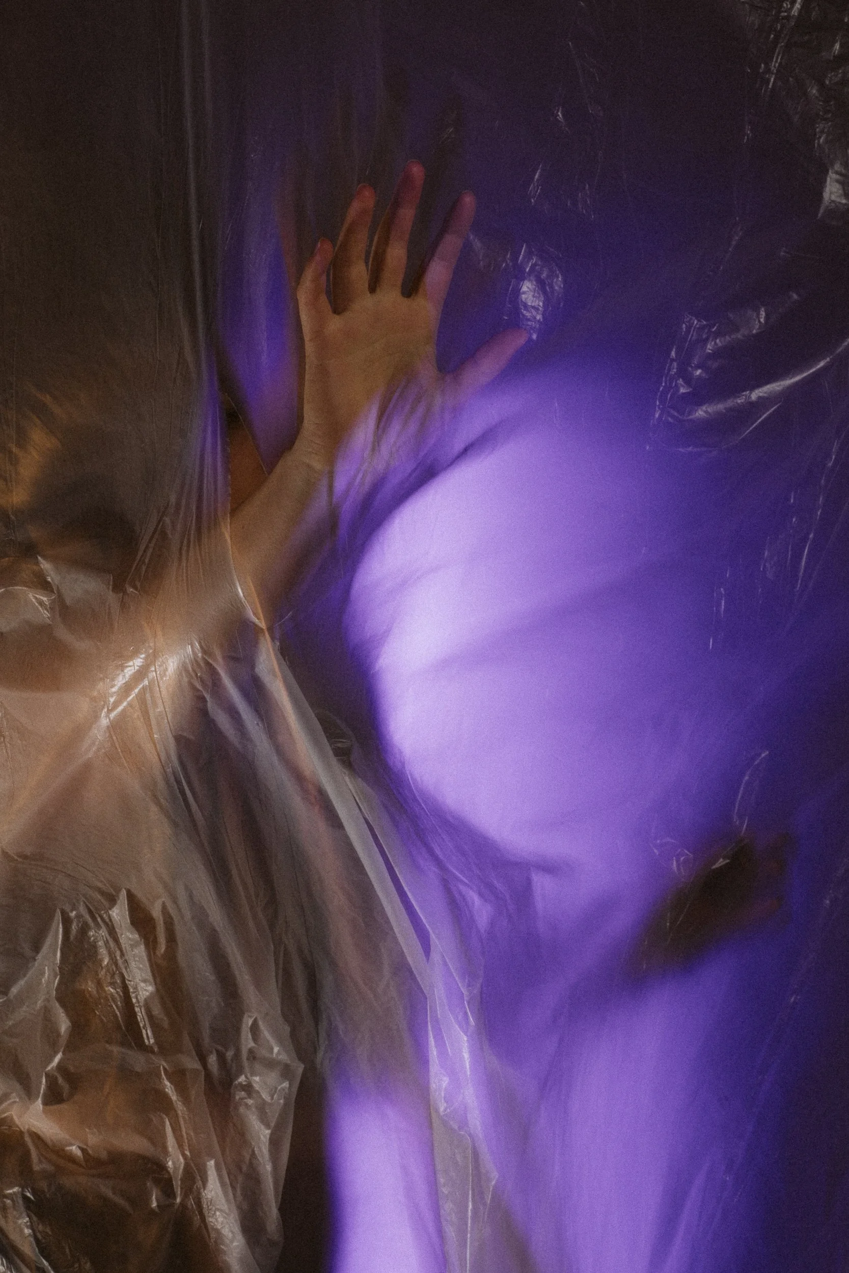 Person's hand pressing against a purple illuminated, crinkled plastic surface.