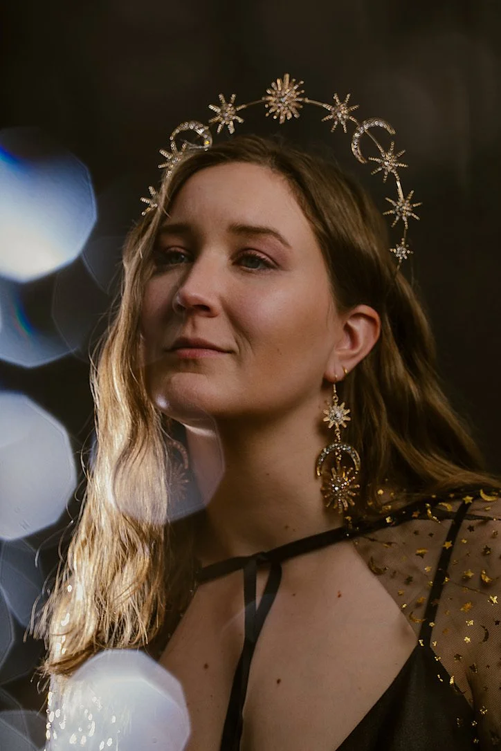 Woman wearing a starry halo and celestial earrings with glowing reflections.