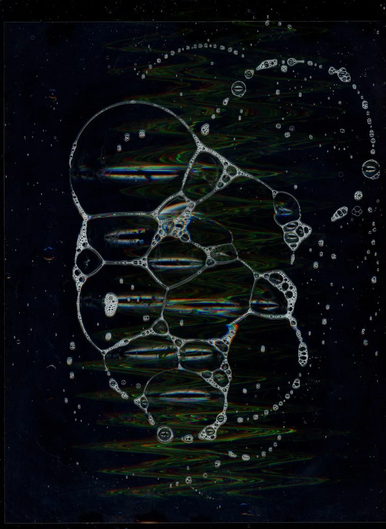 A dark background with interconnected soap bubbles reflecting light and creating iridescent patterns. Created with scanography