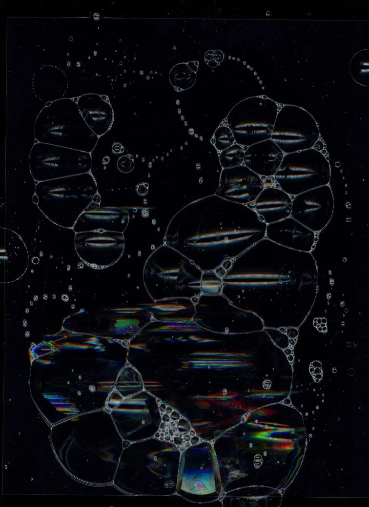 Bubbles forming various connected shapes on a dark background with rainbow reflections. Created with scanography