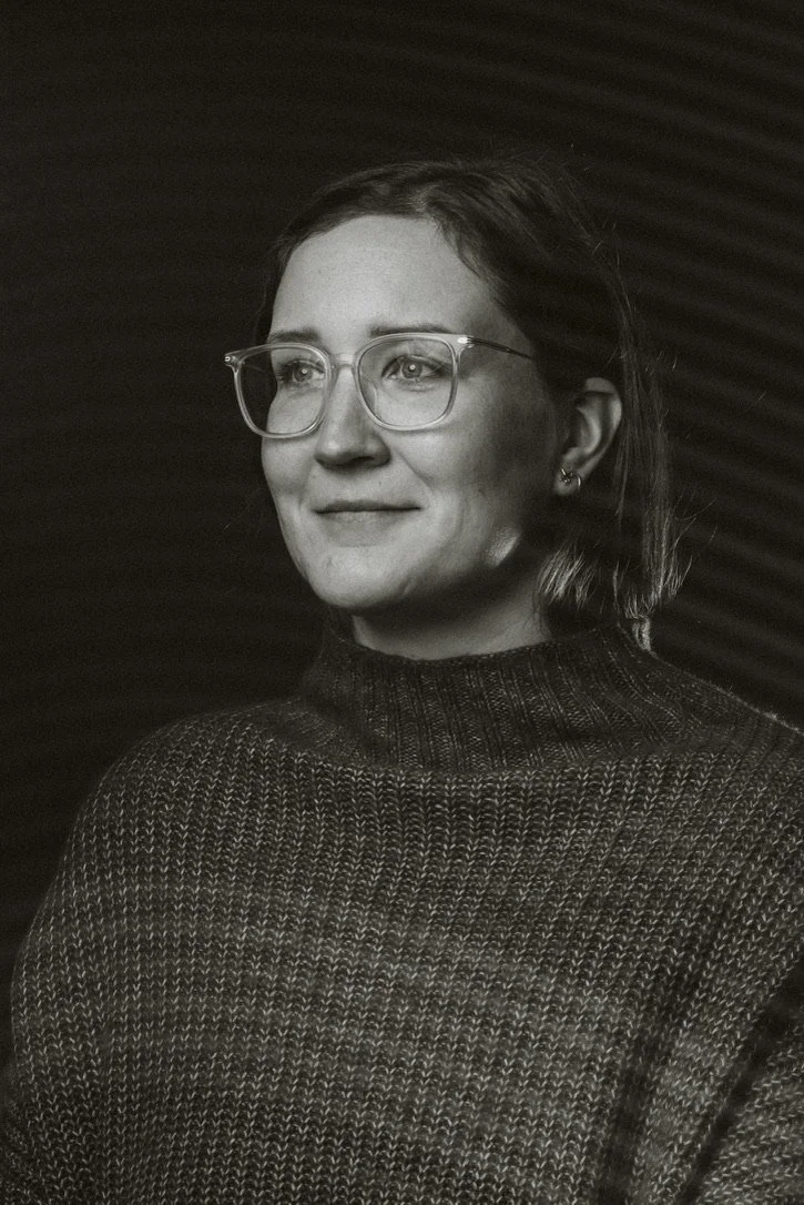 Black and white photo of a person wearing glasses and a sweater, looking to the side.
