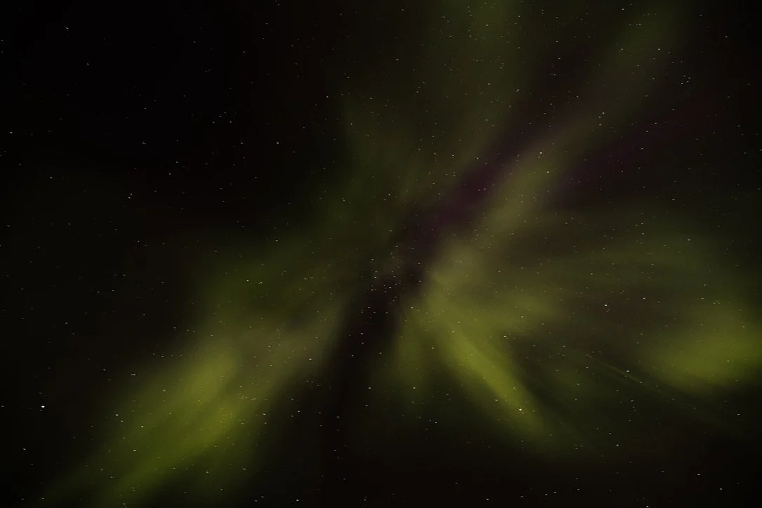 View of the night sky with green aurora and numerous stars.