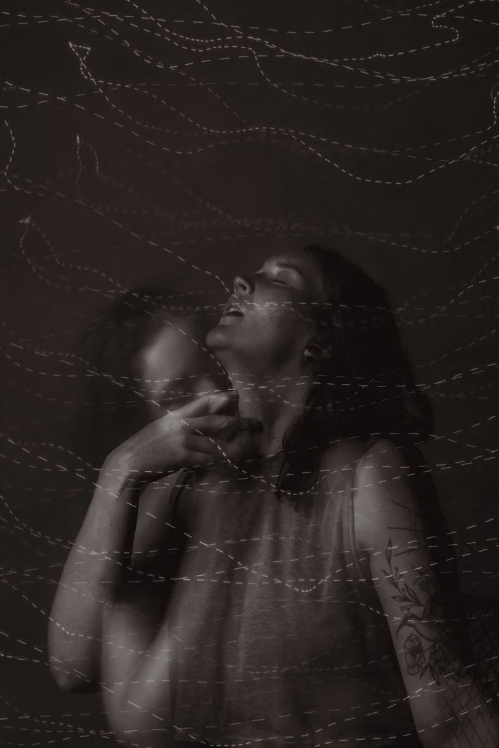 A woman with long hair and tattoos on her arm, with eyes closed and hand near her chin, is surrounded by white dashed lines on a dark background, creating an abstract, artistic effect.