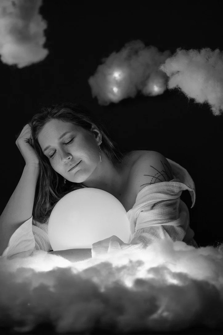 Black and white photo of a woman with a glowing orb, surrounded by cotton clouds.