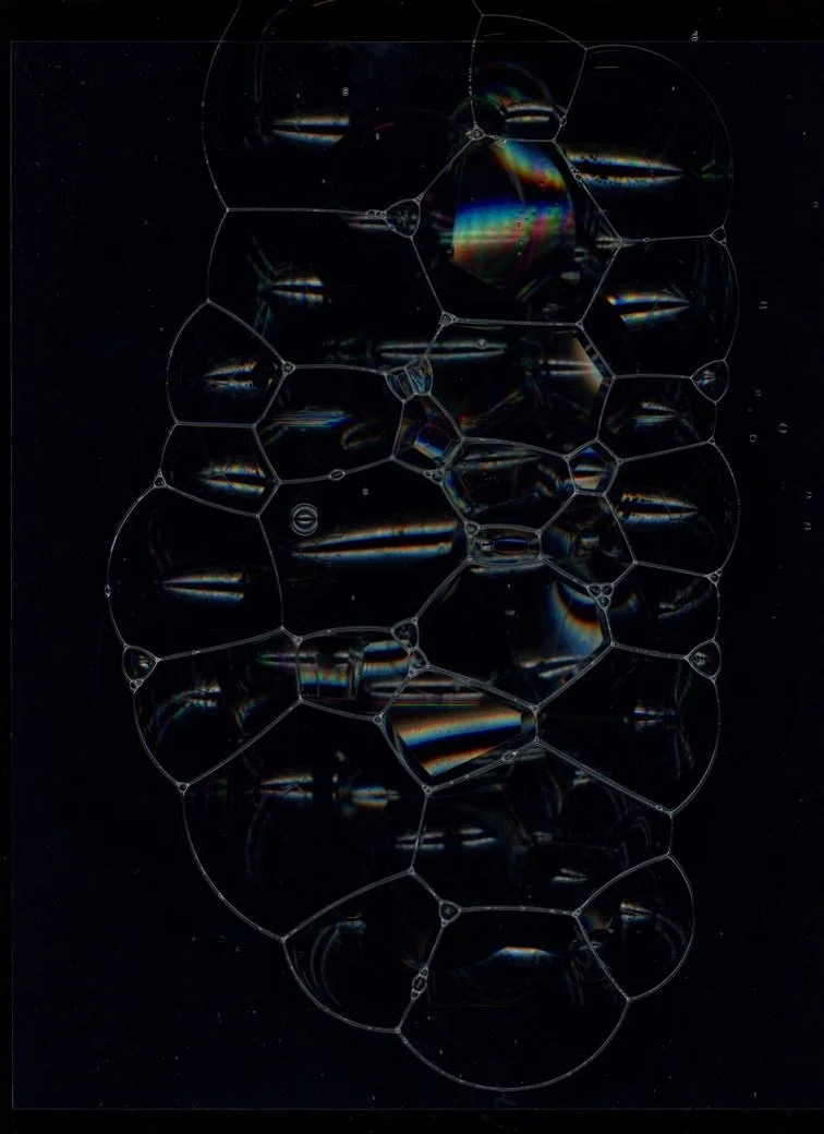 Close-up of soap bubbles forming a honeycomb pattern against a dark background. Created with scanography