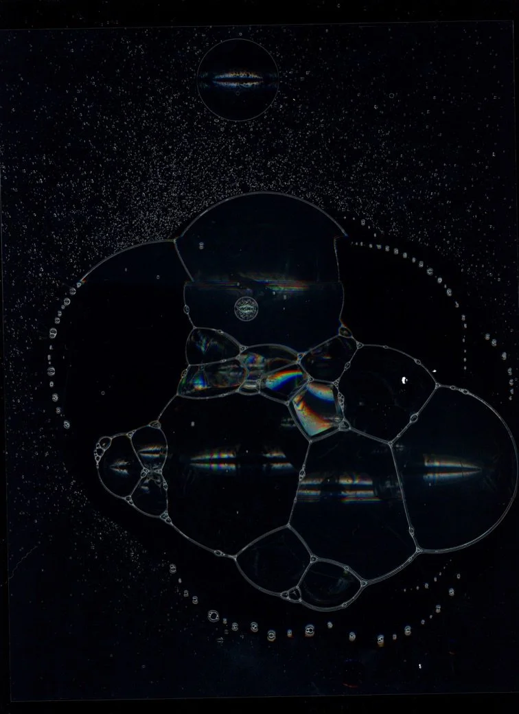 Abstract image featuring soap bubbles of various sizes floating in dark space with stars and seemingly cosmic elements. Created with scanography