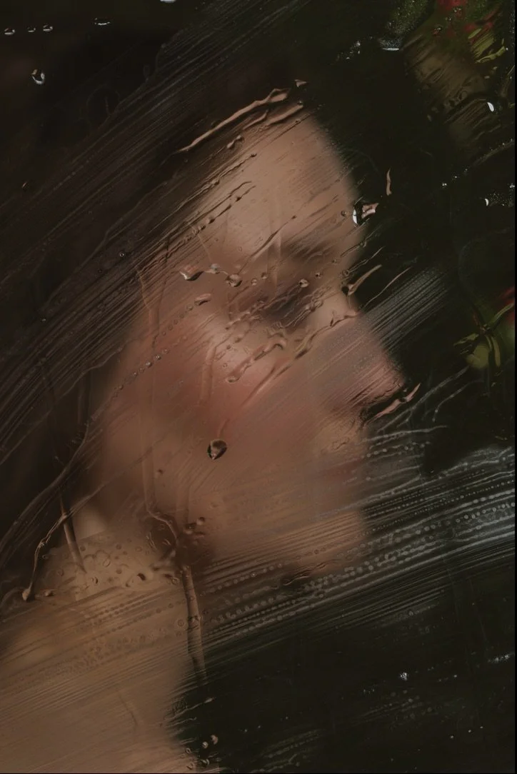 Blurred image of a person seen through a foggy glass with water droplets, obscuring details.
