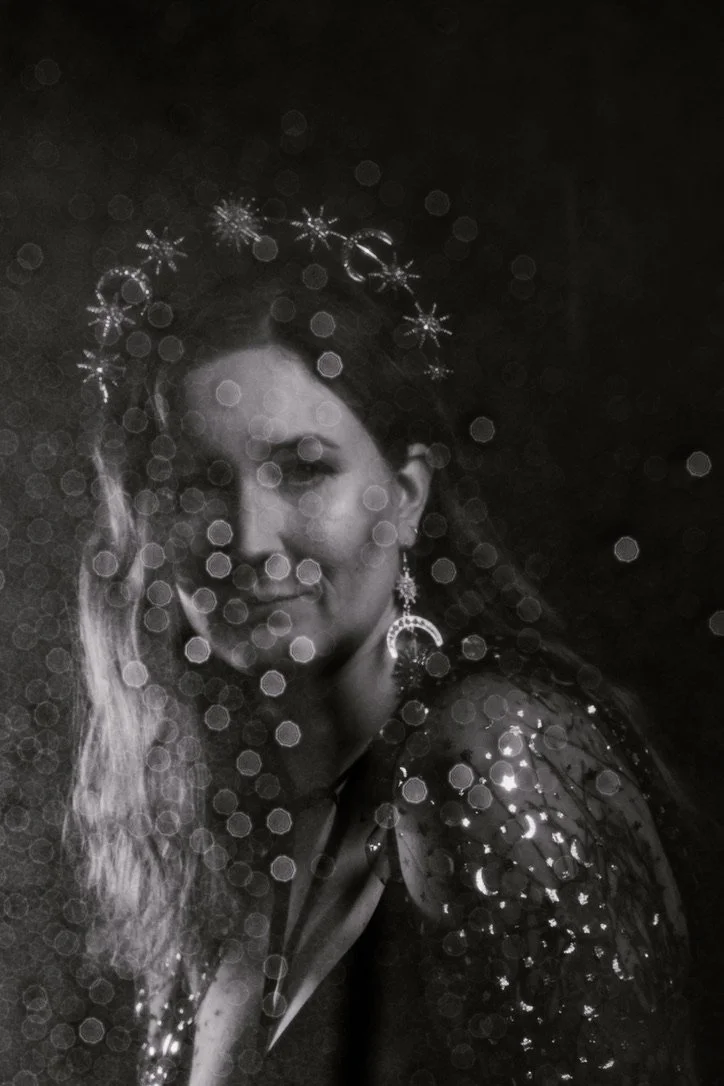 Black and white portrait of a woman with star and moon-themed jewelry, featuring bokeh effect.