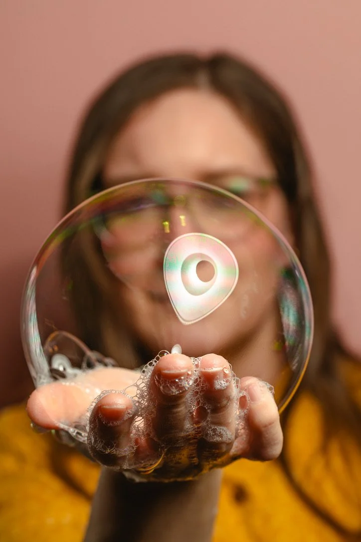 Person holding a soap bubble with a digital icon reflection, focusing on bubble and suds.