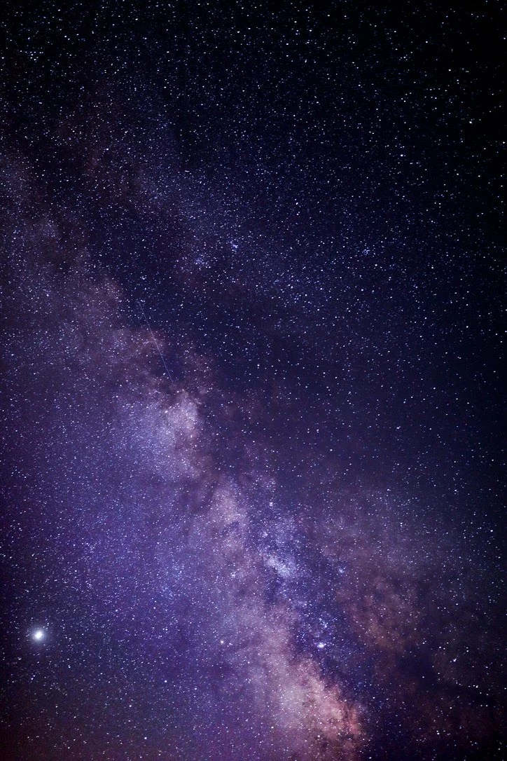 A clear night sky filled with countless stars and the Milky Way galaxy stretching diagonally across the image.