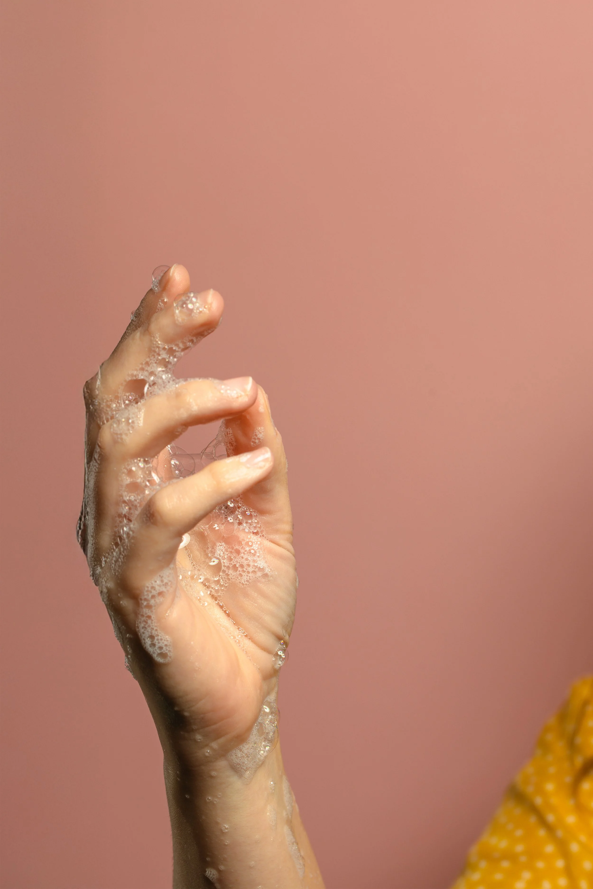 A hand with soapy bubbles against a pink background.