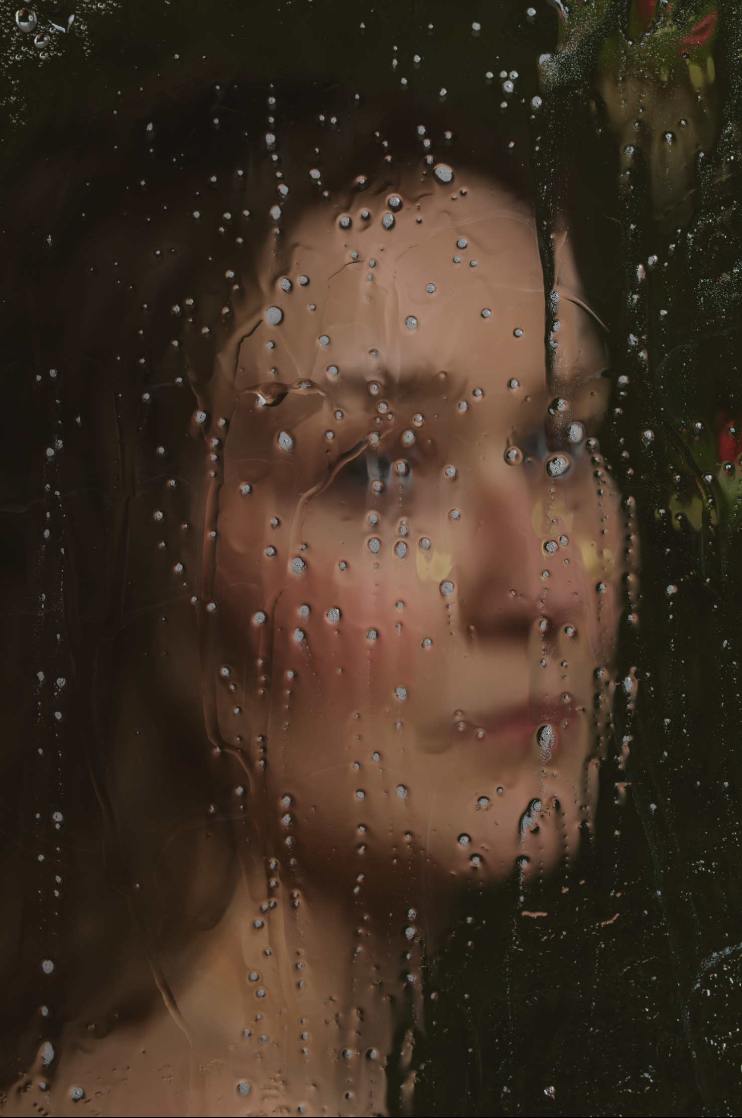 A woman with smooth skin and closed eyes looking through a foggy or wet glass surface with water droplets.