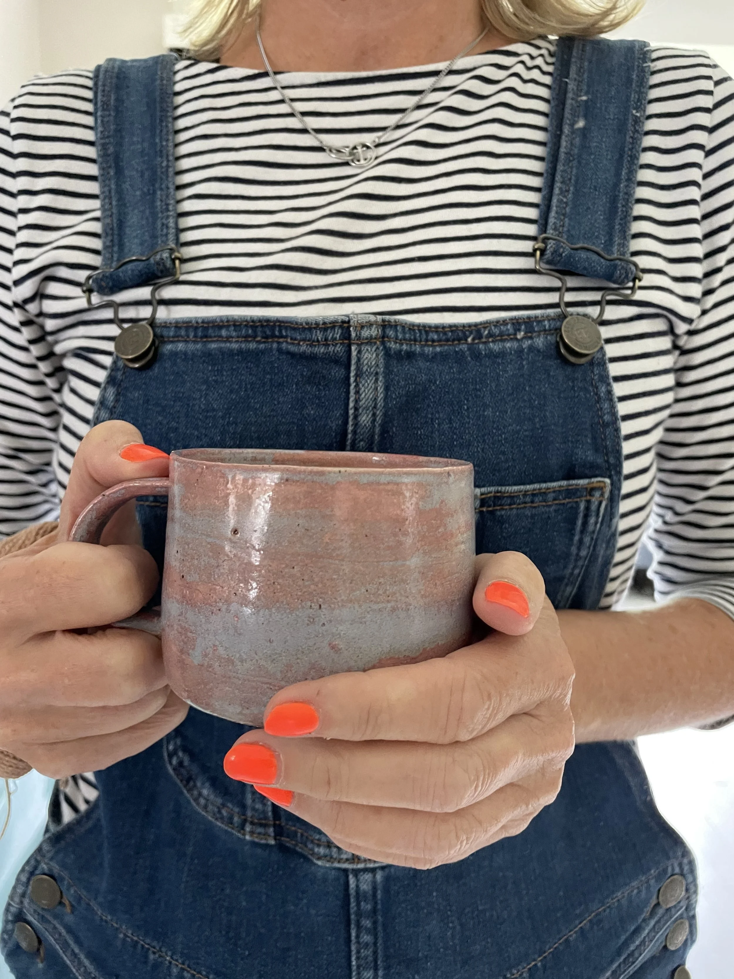 Linda holding  a handmade stoneware ceramic pink sky mug