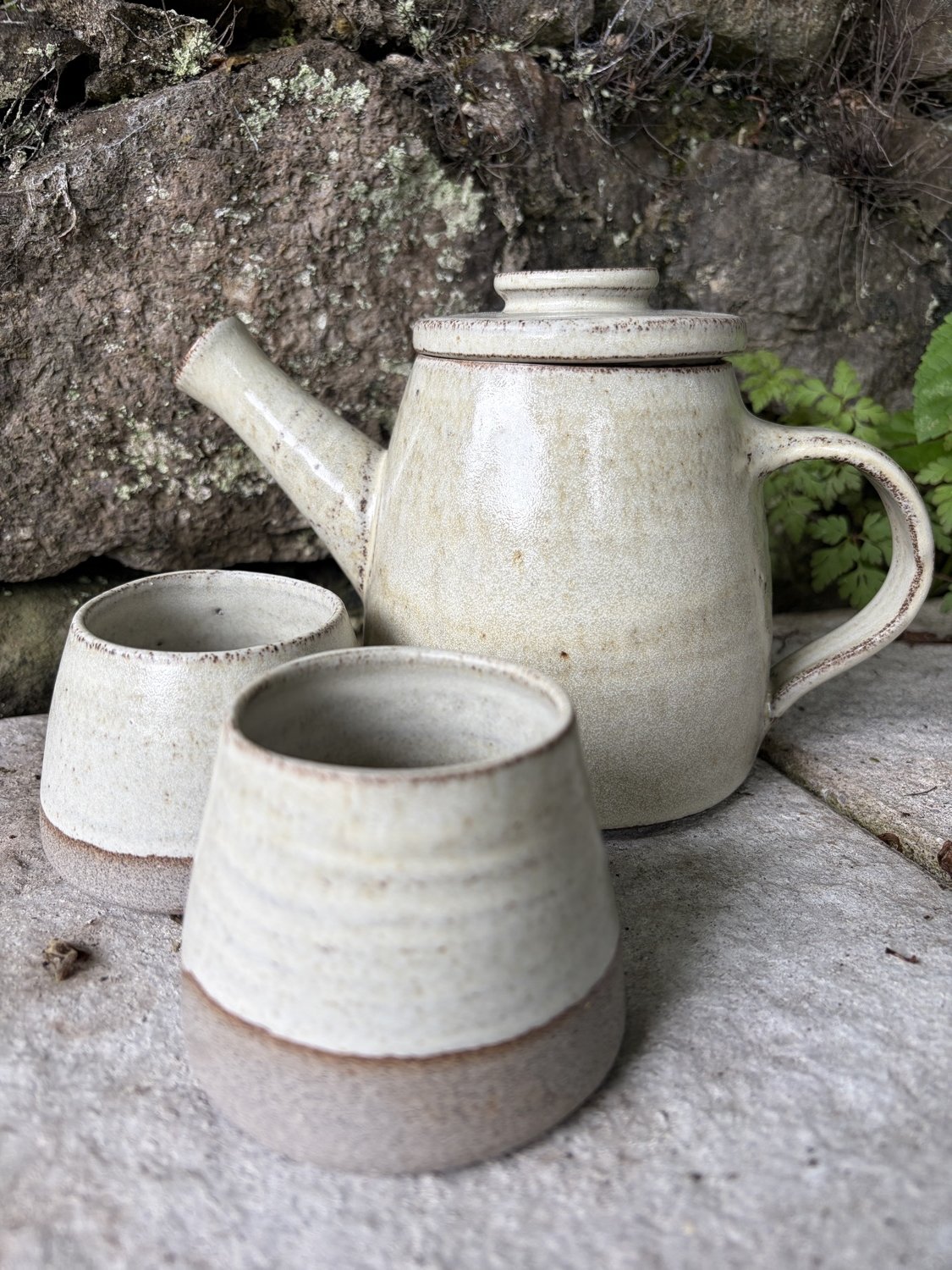 Handmade wheel thrown stoneware handleless cup grey clay vanilla glaze pictured with a matching teapot