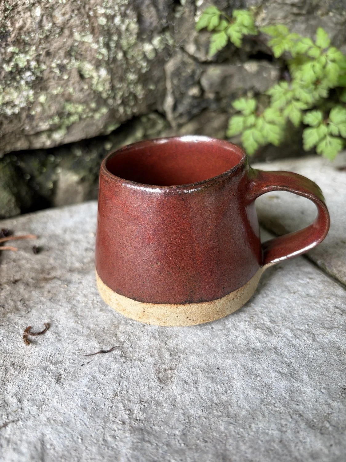 Handmade stoneware small cup in a molten glaze pictured on a wall