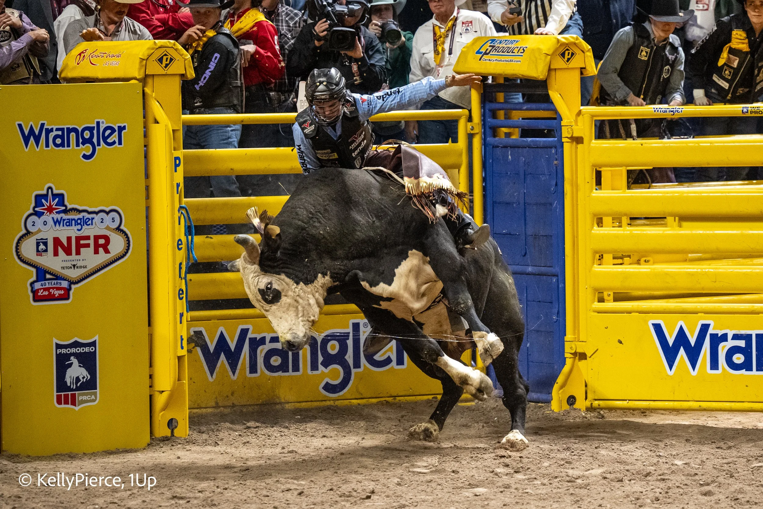 A cowboy on a bucking bull during a rodeo event with spectators and photographers in the background.