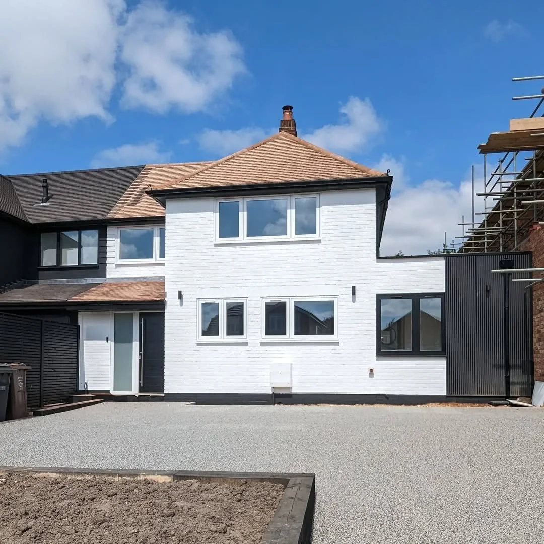 Newly renovated white brick house with multiple windows, a black gate, and a gravel courtyard under a blue sky with clouds.