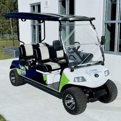 Green and white golf cart with black seats and a roof parked outside a building.