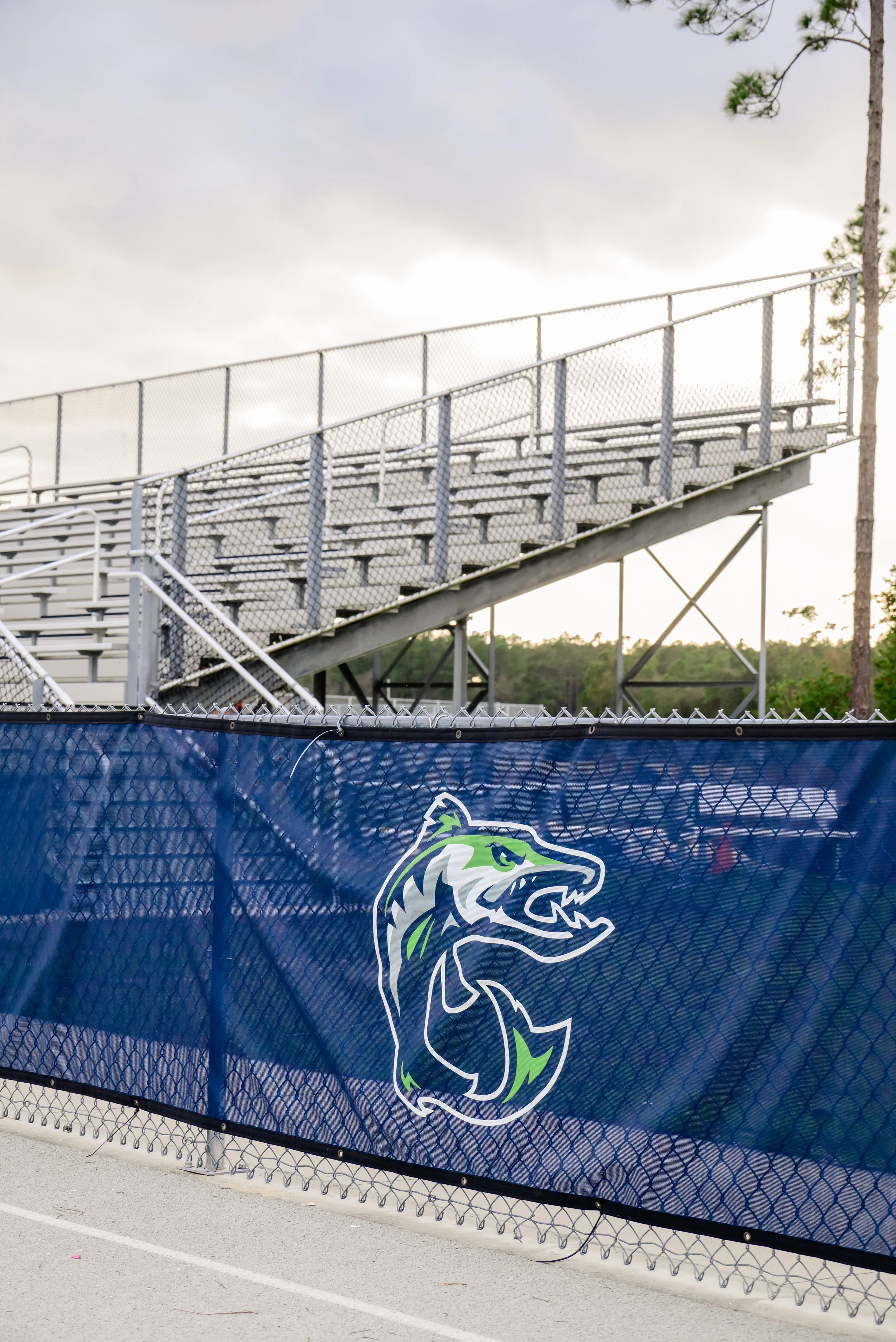 Empty stadium bleachers behind a chain-link fence with a sports team logo depicting a fierce wolf head on it.