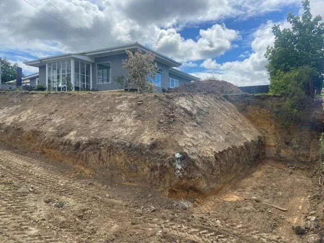 House on a hill with a large excavation and dirt slope in the foreground, partly cloudy sky in the background.