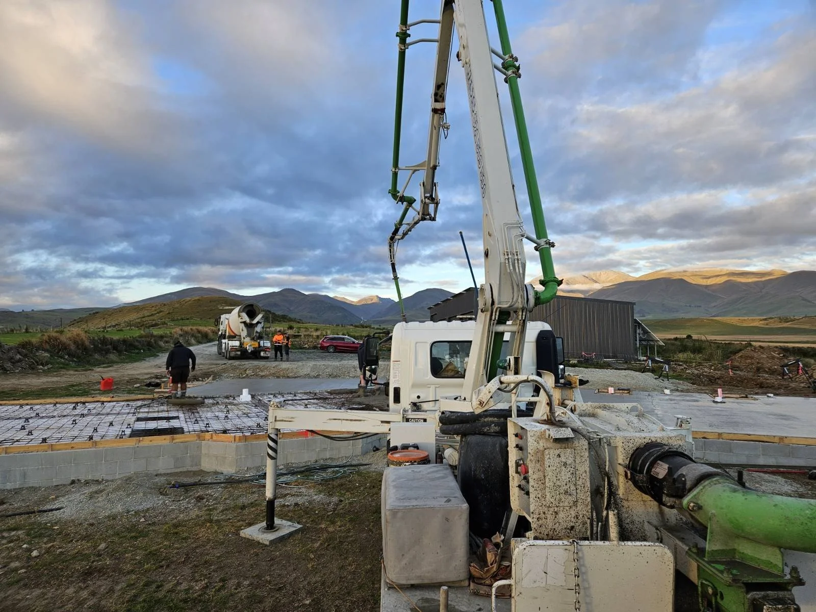 Construction site with concrete pouring machinery, workers, and a scenic mountain landscape in the background.