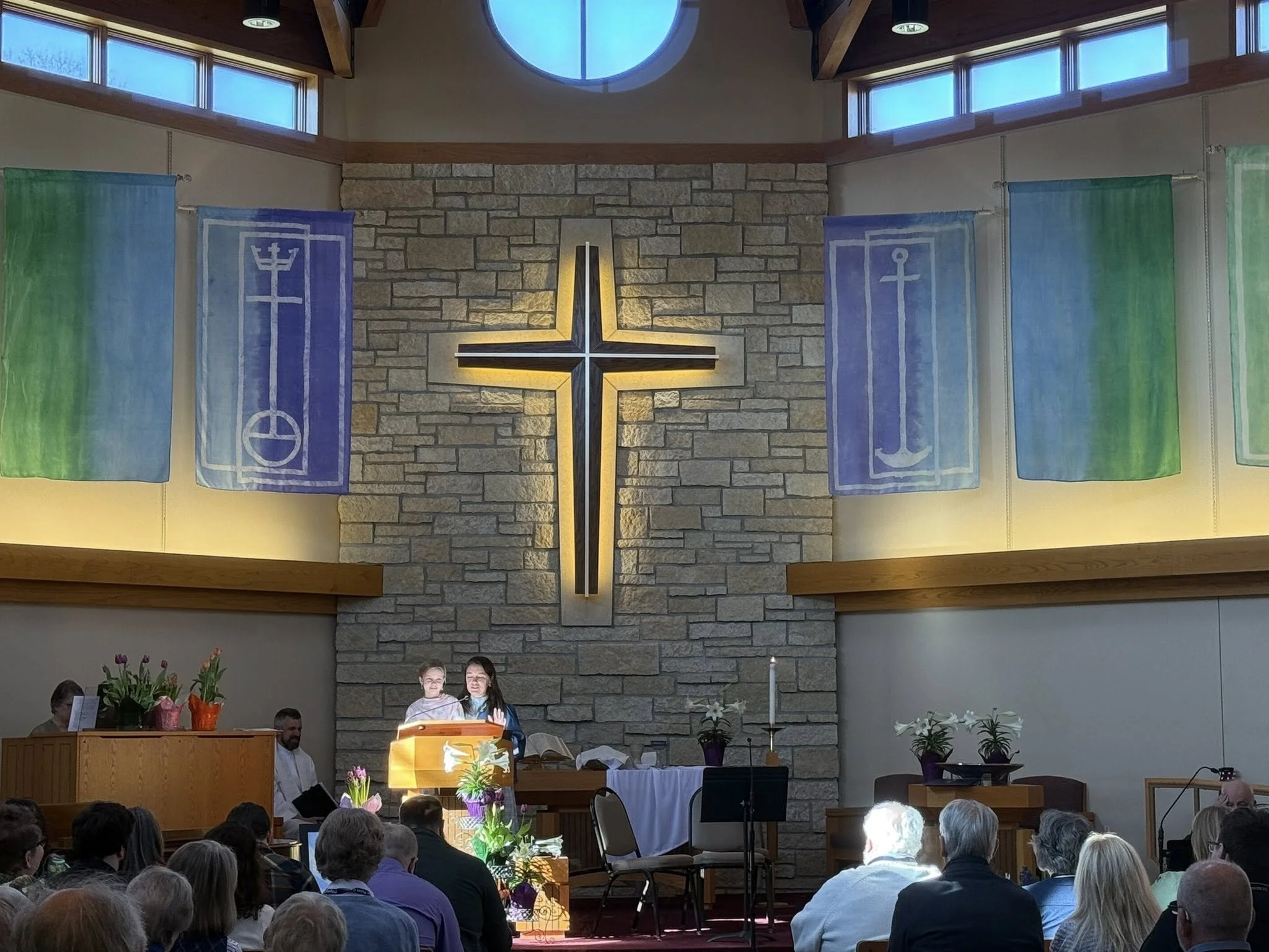 Congregation watching mother and little daughter speak at the front of the church.