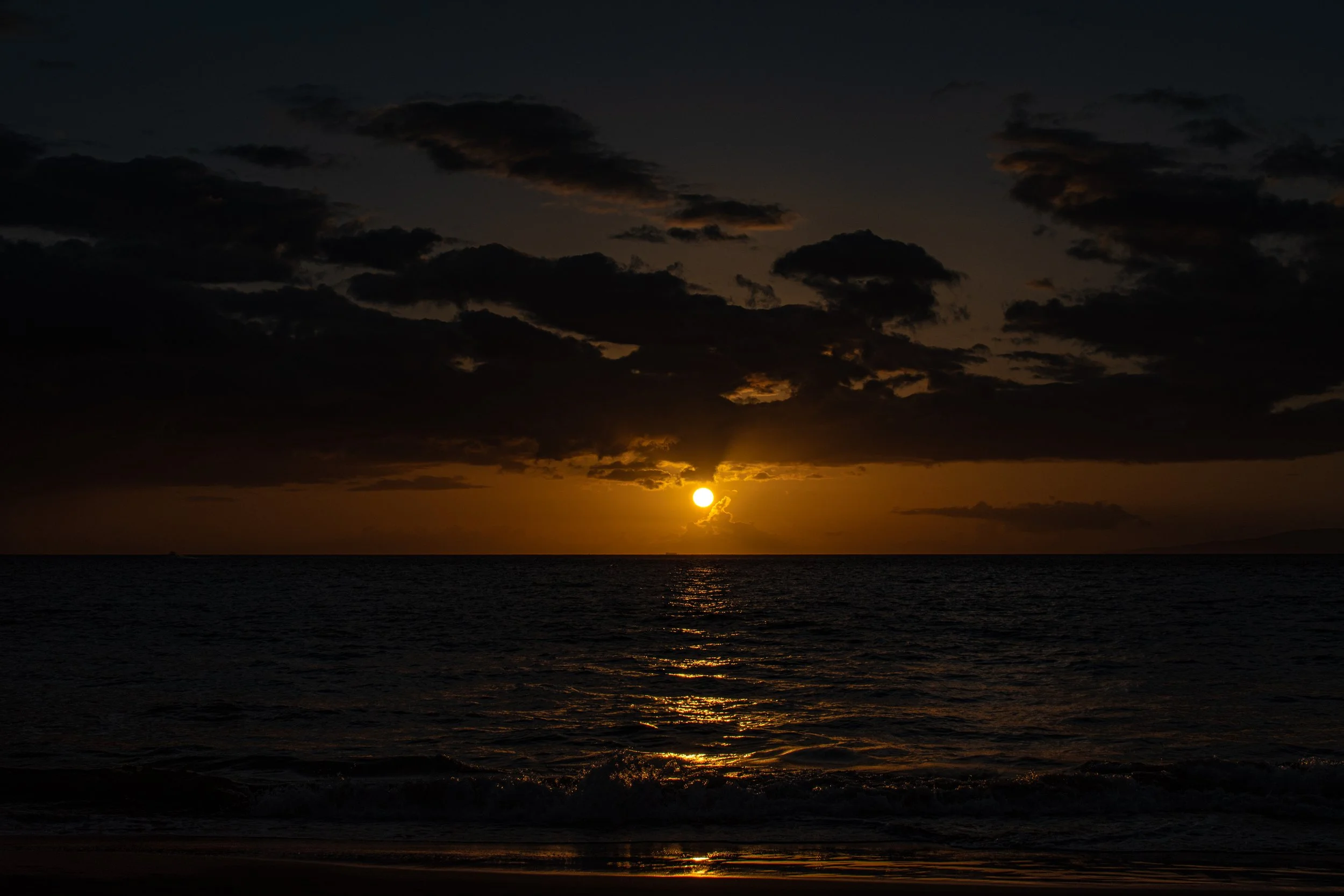 Sunset over the ocean with dark clouds in the sky.