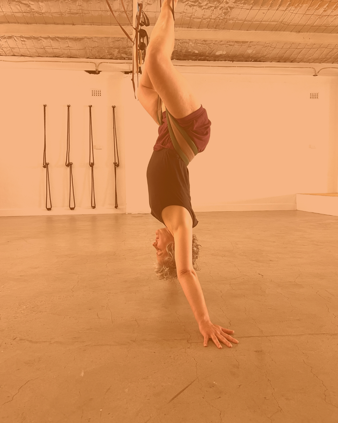 Person practicing yoga in a downward dog pose with a strap around their hips, head resting on a folded blanket on a yoga mat.