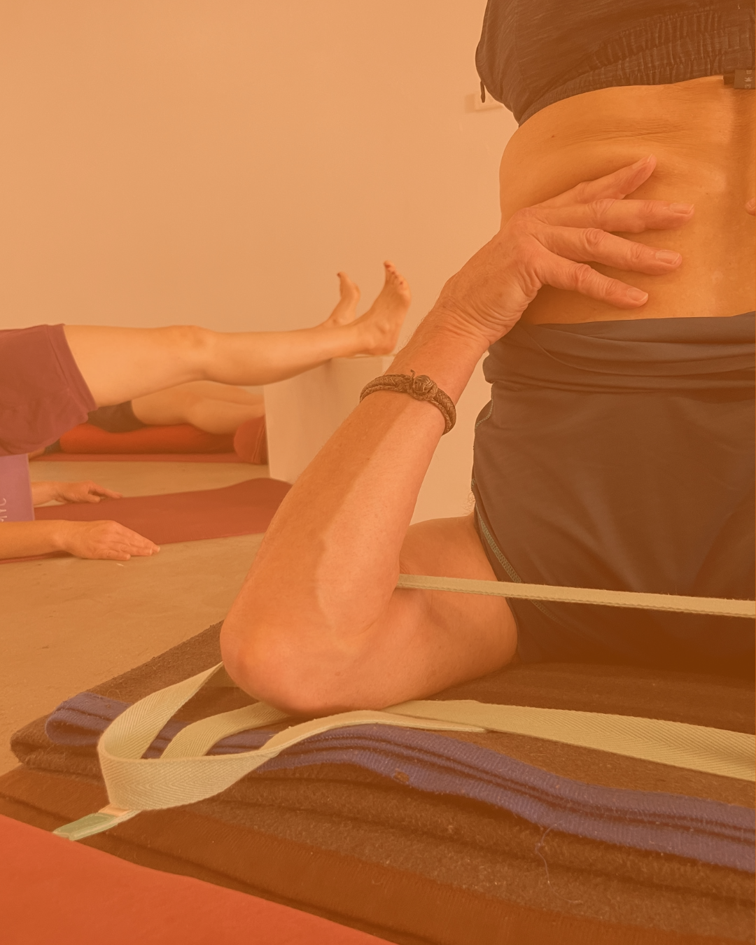 Person practicing a yoga pose with props including a wooden arch, bolsters, and blankets on a wooden floor.