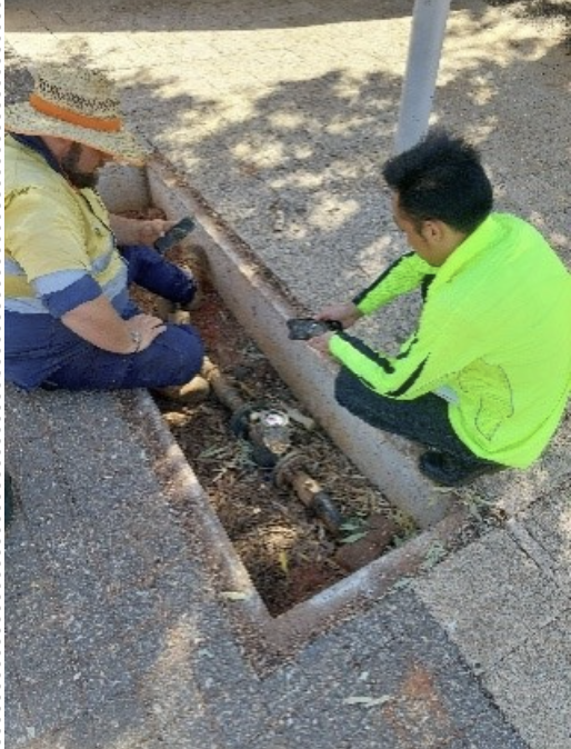 Engineered Efficiency workers inspecting a meter embedded in the sidewalk at street level.