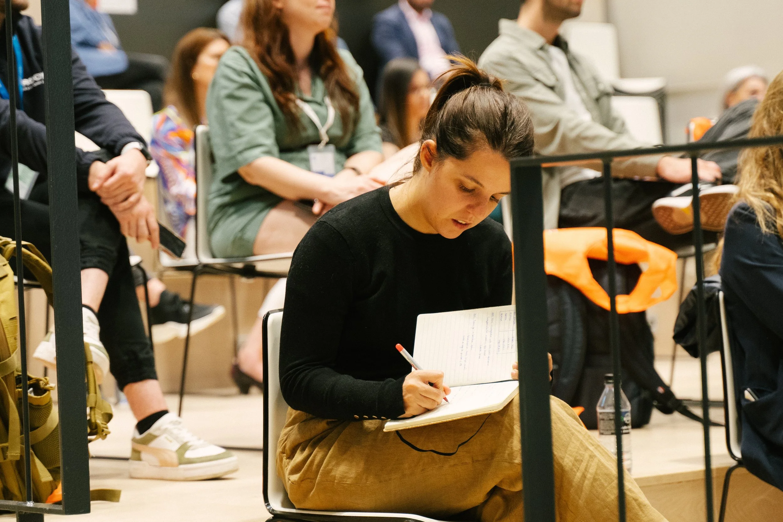 A young woman taking notes in a notebook while attending a conference.