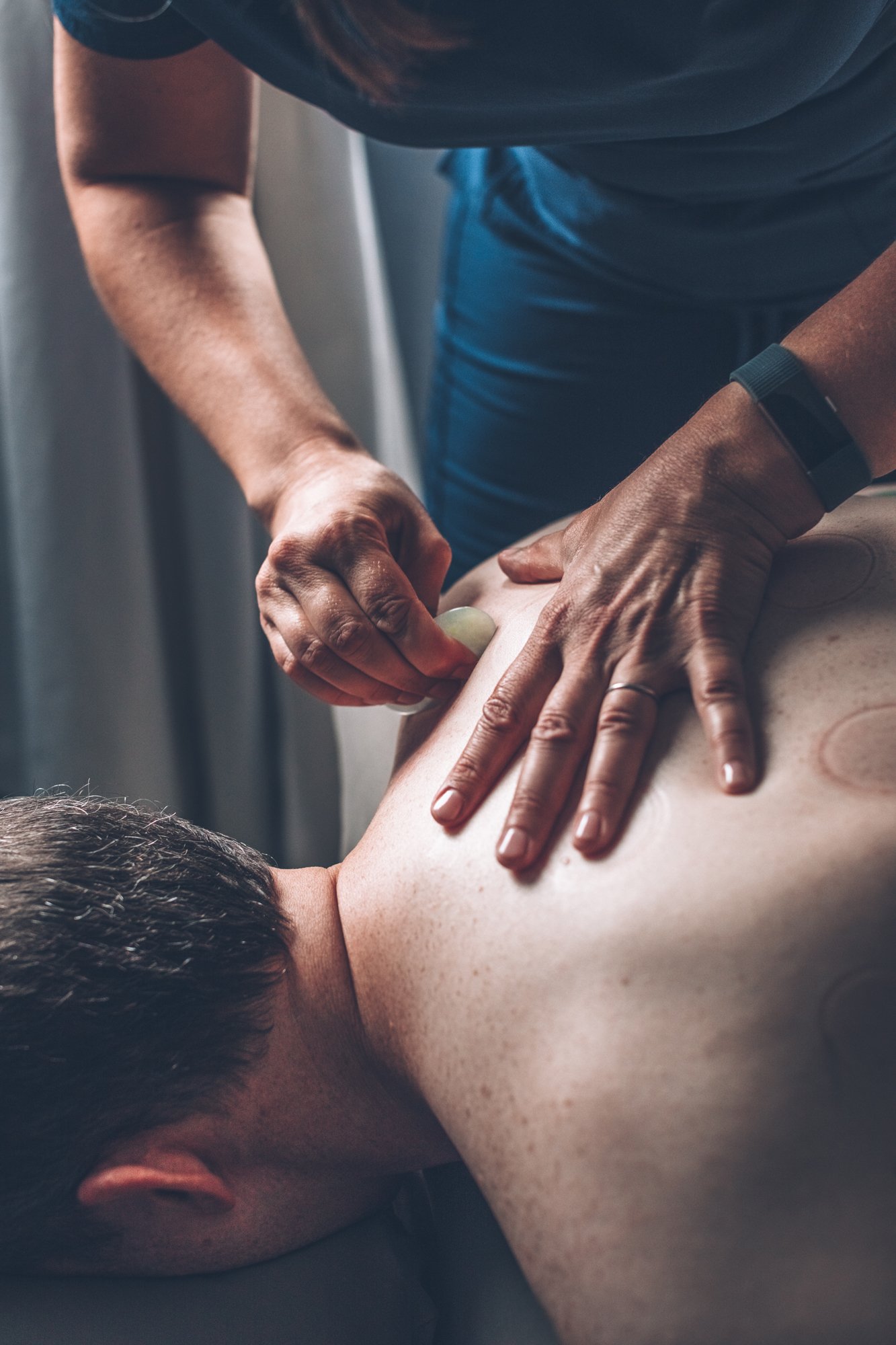 Practitioner using a gua sha tool across a patient's upper back and shoulder.