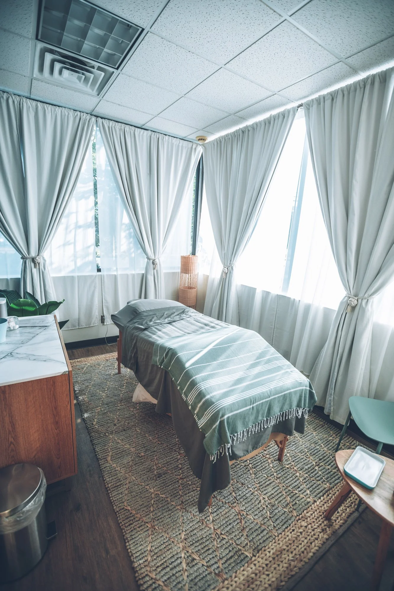 A serene acupuncture treatment room with a table, soft linens, and natural light through sheer curtains.