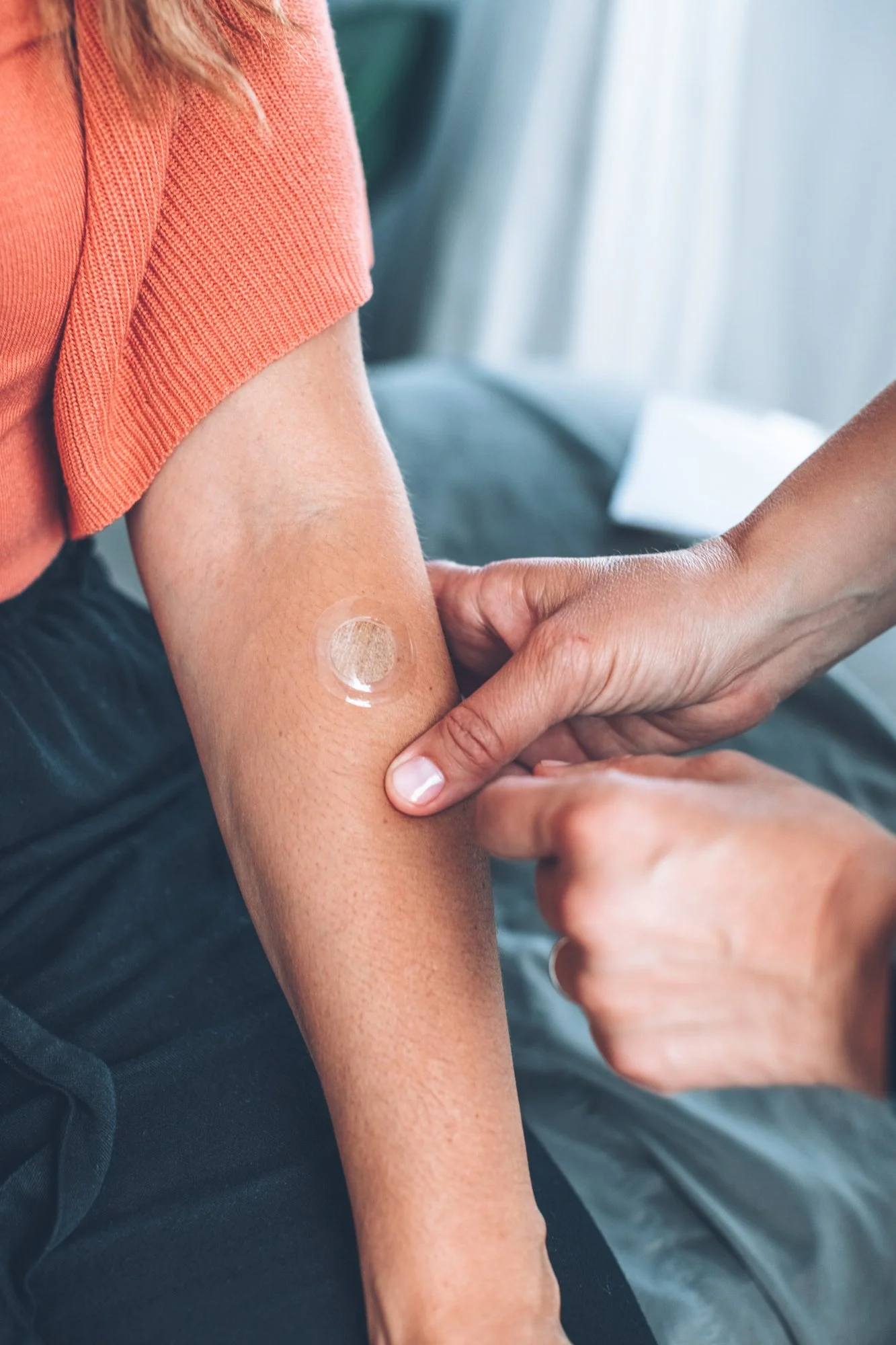 Person receiving a vaccination shot in their upper arm, with a circular adhesive bandage on the site of the injection.
