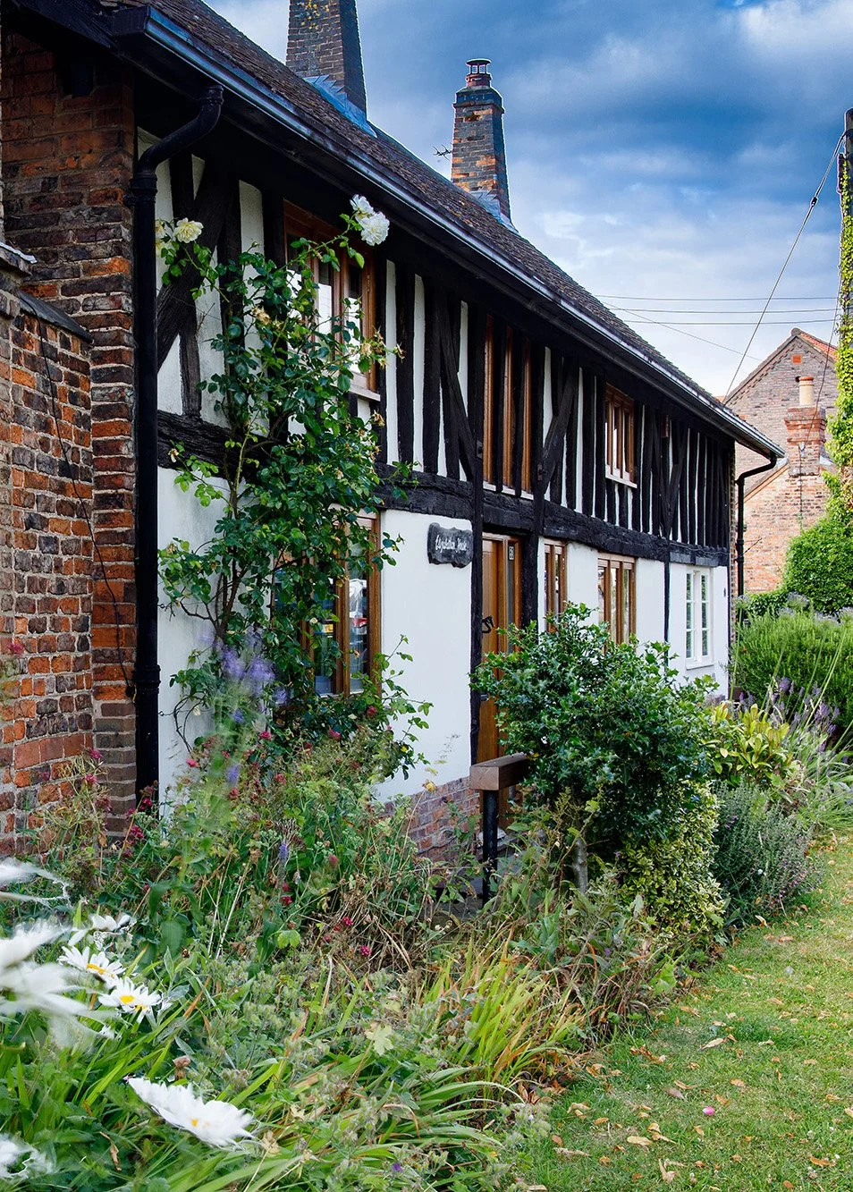 A black-and-white half-timbered house with a garden full of flowering plants and bushes.