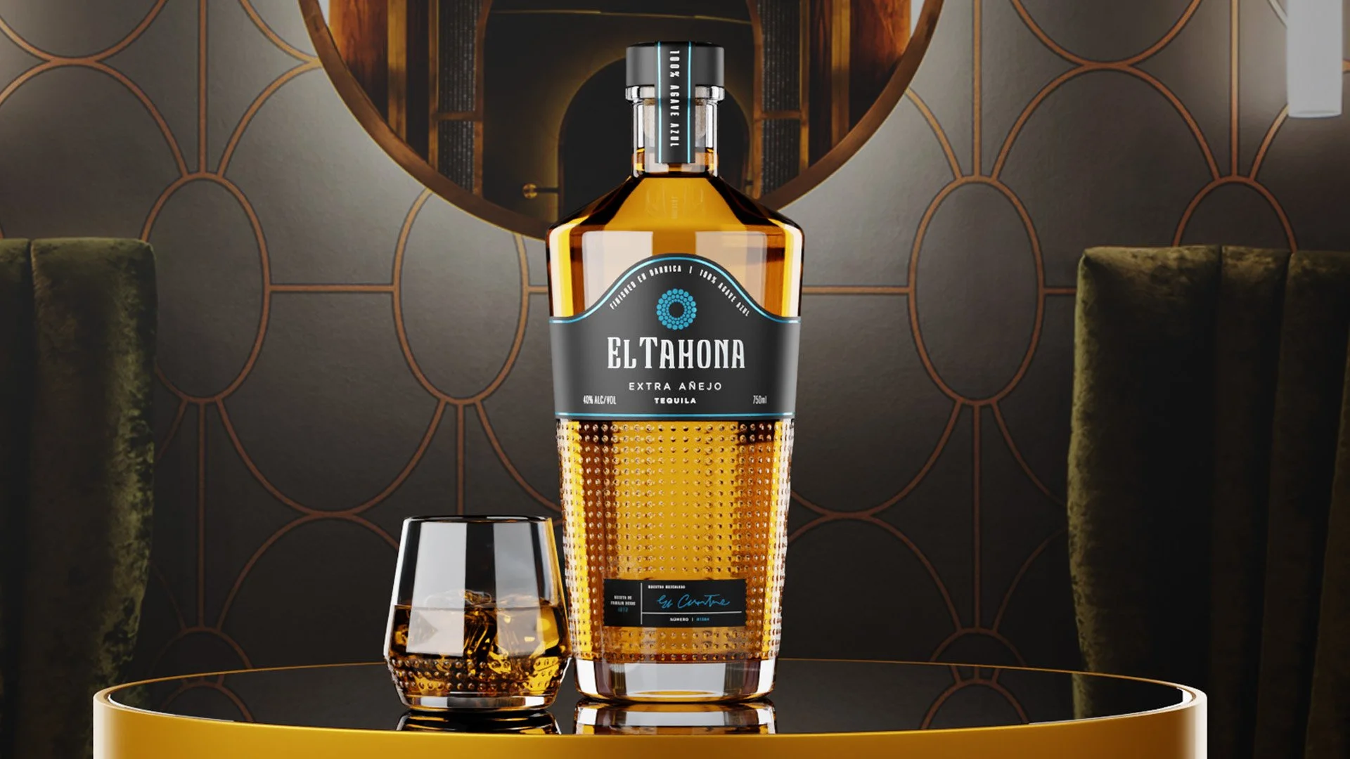 A bottle of El Tahoma extra añejo tequila and a glass with ice on a black-and-gold table in an elegant room with a round mirror and green velvet chairs.