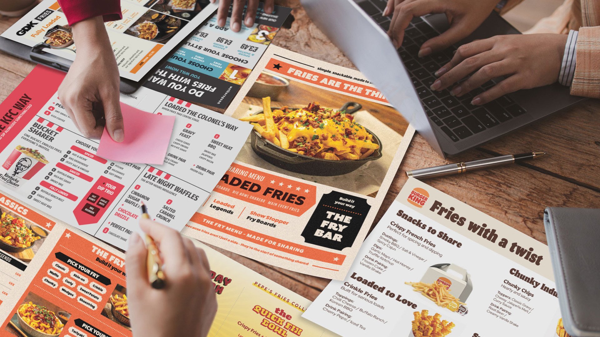 Several people reviewing menus for fried foods and snacks at a wooden table, including items like loaded fries, chicken, buffalo wings, and crispy French fries.