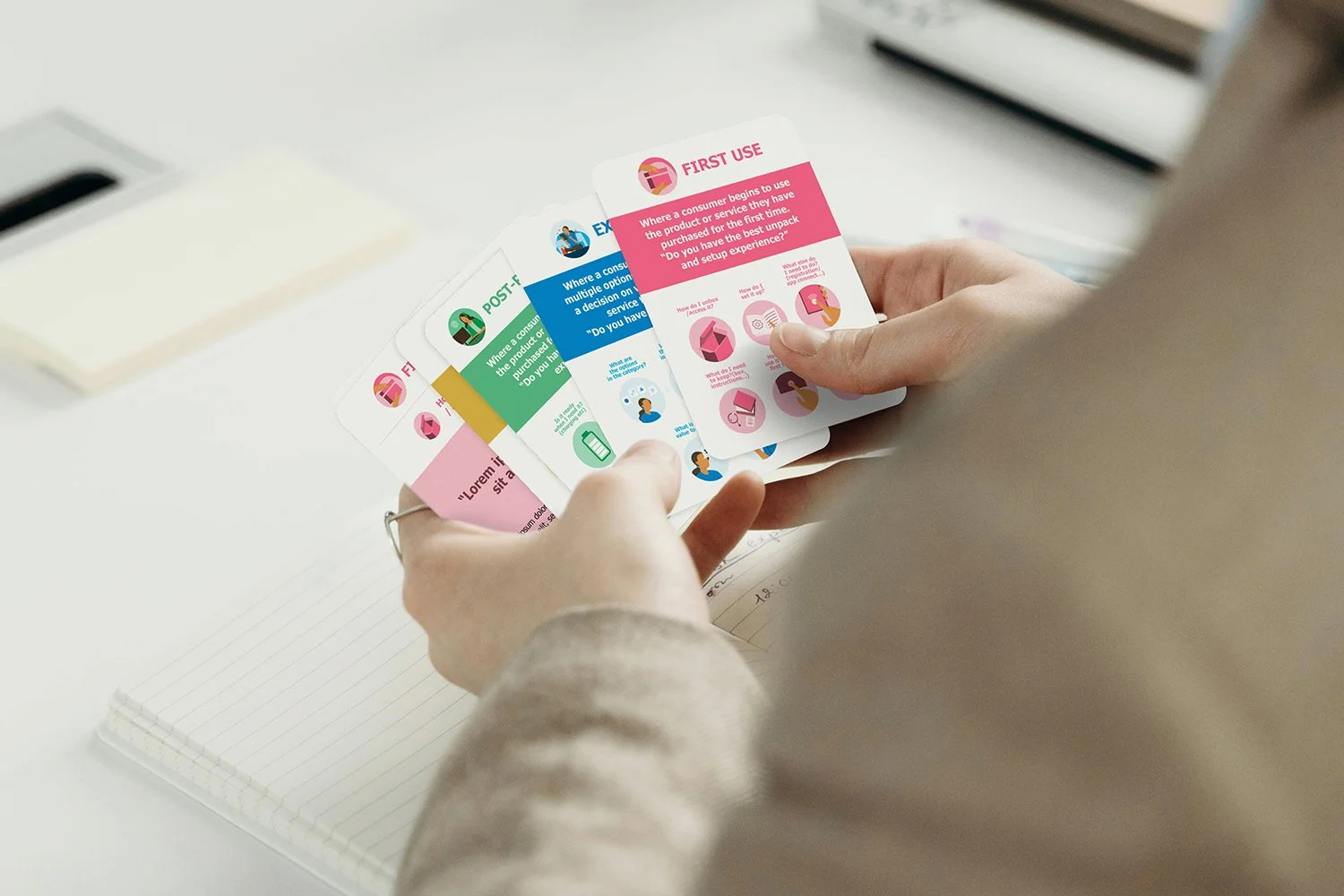 Person holding colorful cards with instructions, sitting at a desk with a spiral notebook and a stack of books in the background.