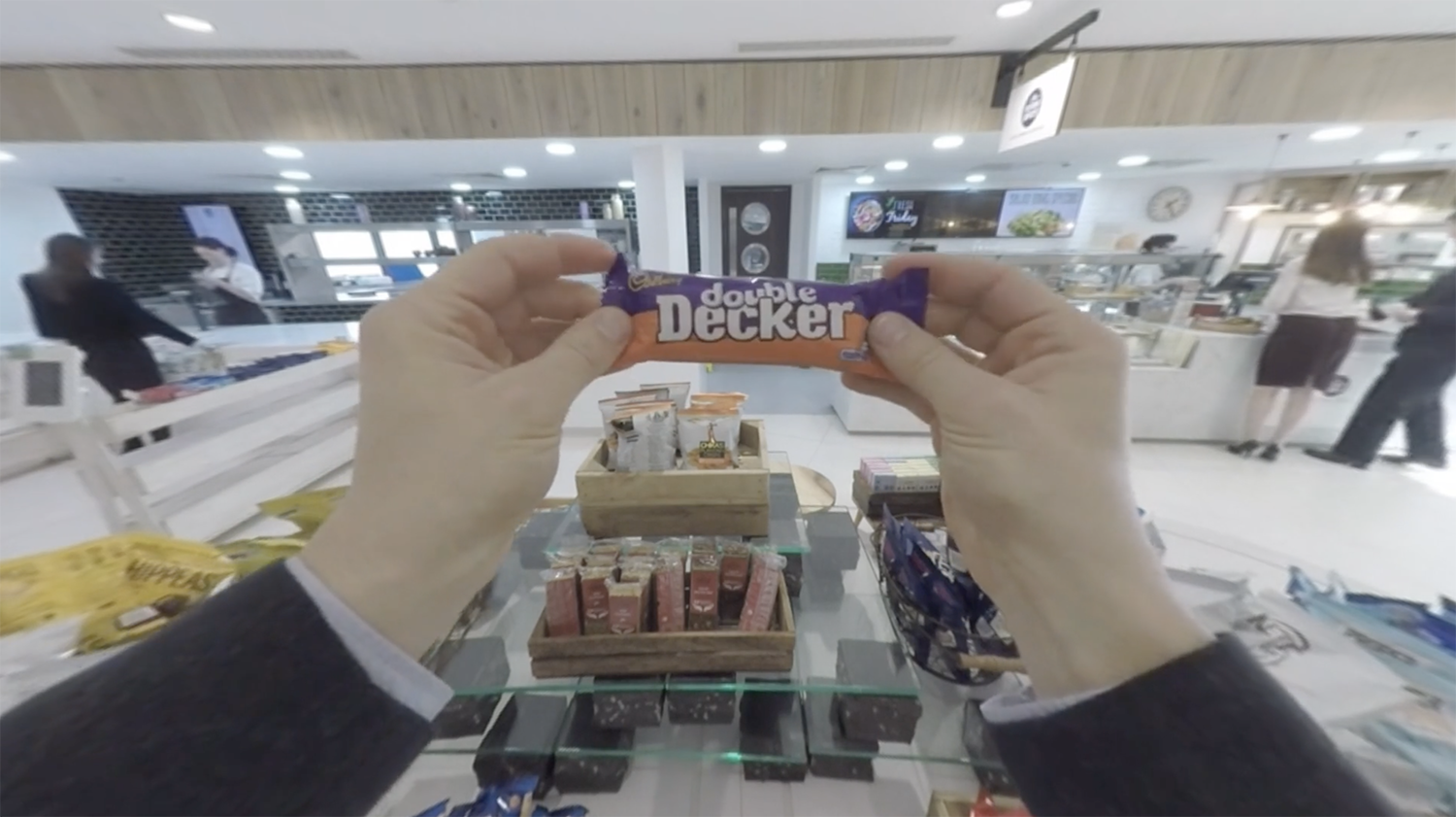 Person holding a Double Decker chocolate bar in a store aisle with various other snack items on display.