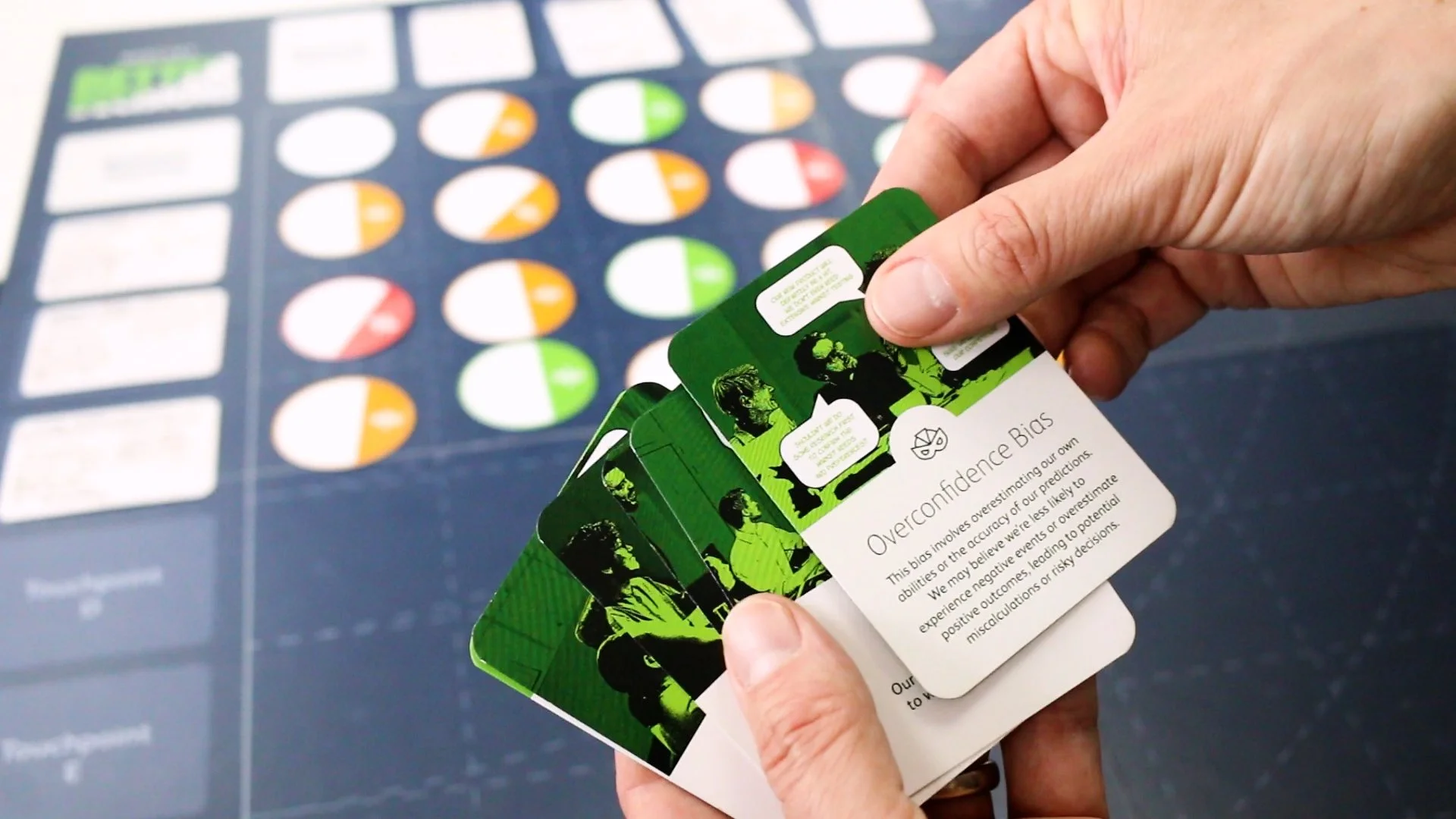 A person holding a stack of cards with graphics and text about cognitive biases, specifically about overconfidence bias, with a chart of colored circles in the background.