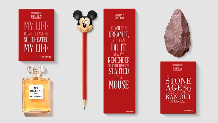 Disney-themed desk accessories including a Mickey Mouse pencil, a red inspirational quote book, a pink stone, a bottle of Chanel No. 5 perfume, and another red quote book.